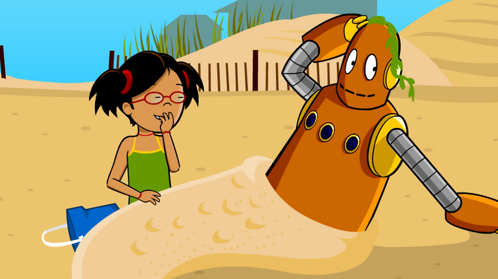 Annie and Moby are playing in the sand at the beach. Annie has buried Moby's legs in sand to make Moby look like a mermaid. Moby poses while they giggle.