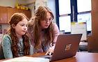 Teacher and student work together on laptop in a classroom setting.