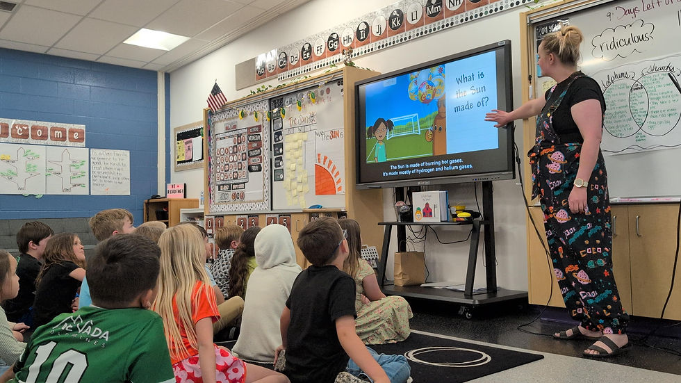 A teacher in colorful pants points to a screen showing a sun quiz to attentive students in a vibrant classroom with educational posters.