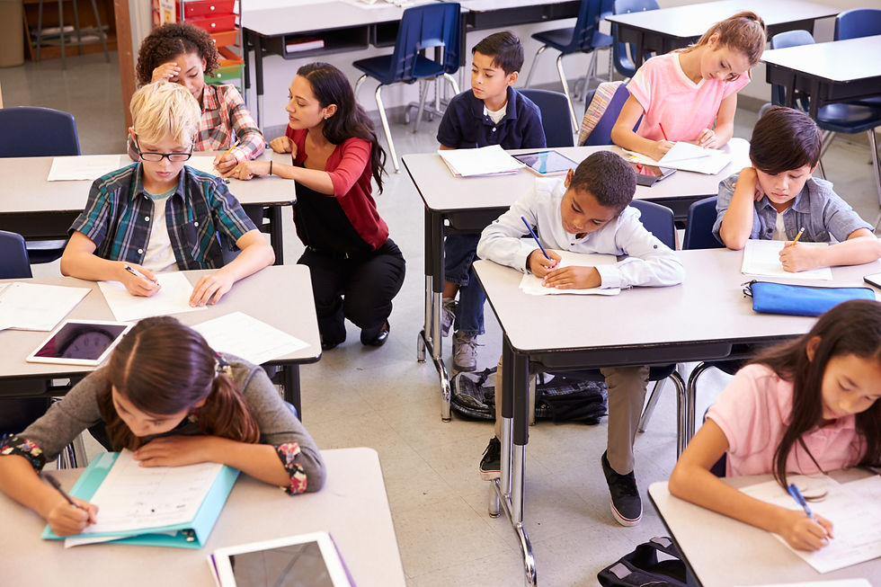 Classroom photography: students are writing at their desks while the teacher observes their work.