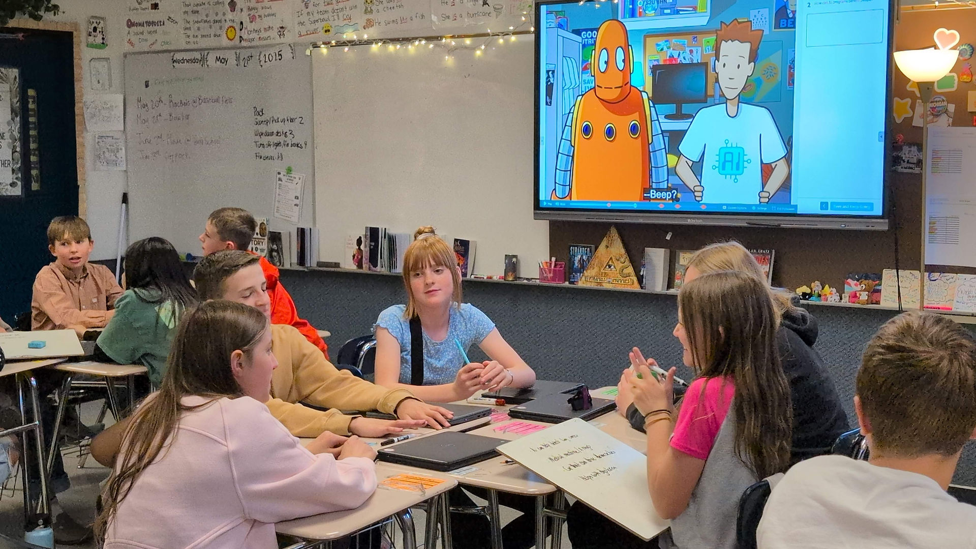 Middle school students sit in clusters of desks for group work. A BrainPOP 3-8 movie with Tim and Moby is on a smart board in the background. 